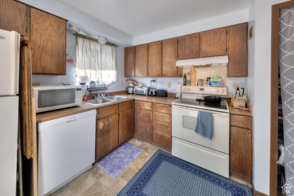 Kitchen featuring a sink, extractor fan, brown cabinetry, and white appliances