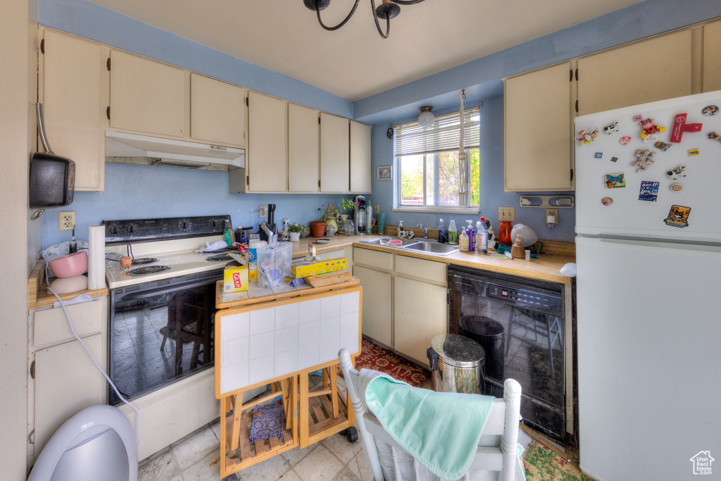 Kitchen with a sink, under cabinet range hood, cream cabinetry, electric range oven, and freestanding refrigerator
