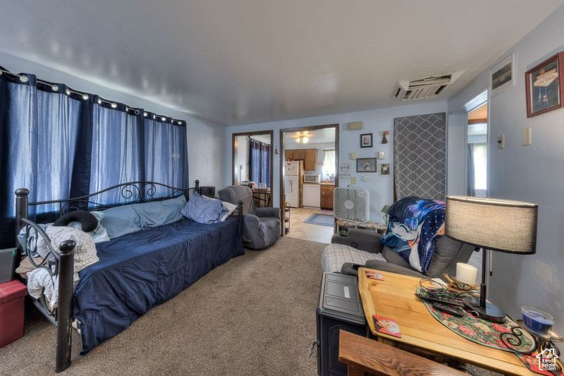 Carpeted bedroom featuring visible vents, freestanding refrigerator, and ensuite bathroom