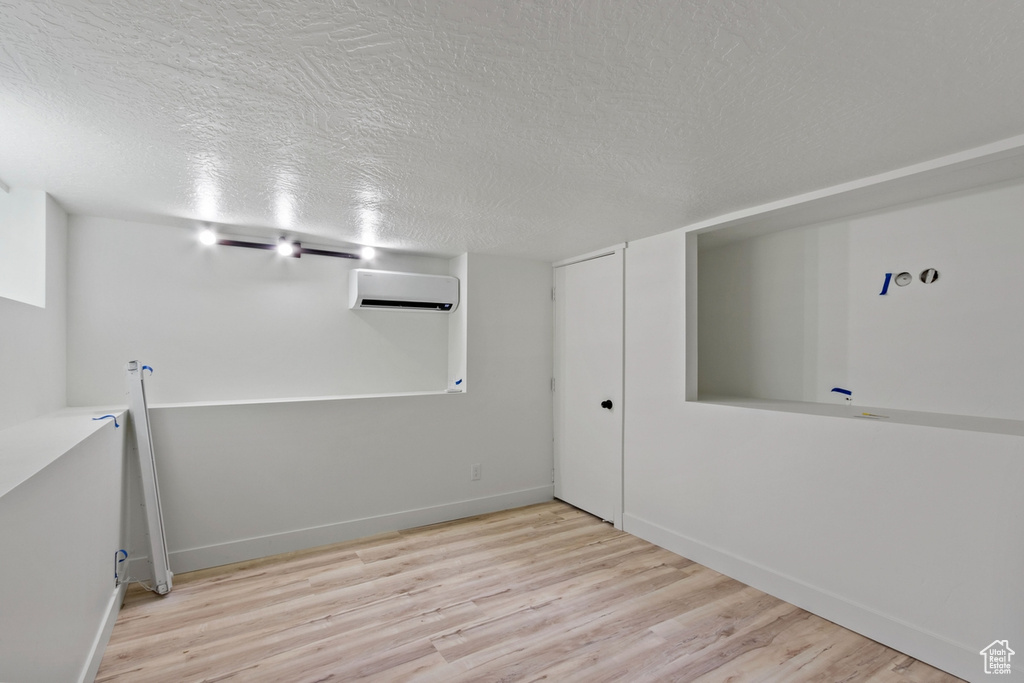 Spare room with baseboards, a textured ceiling, an AC wall unit, and wood finished floors