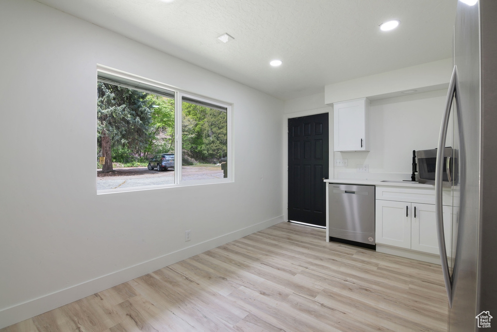 Kitchen featuring baseboards, appliances with stainless steel finishes, white cabinets, and light wood finished floors