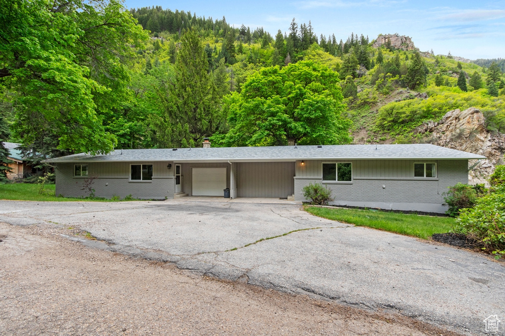 Ranch-style home featuring brick siding, an attached carport, a chimney, a garage, and driveway