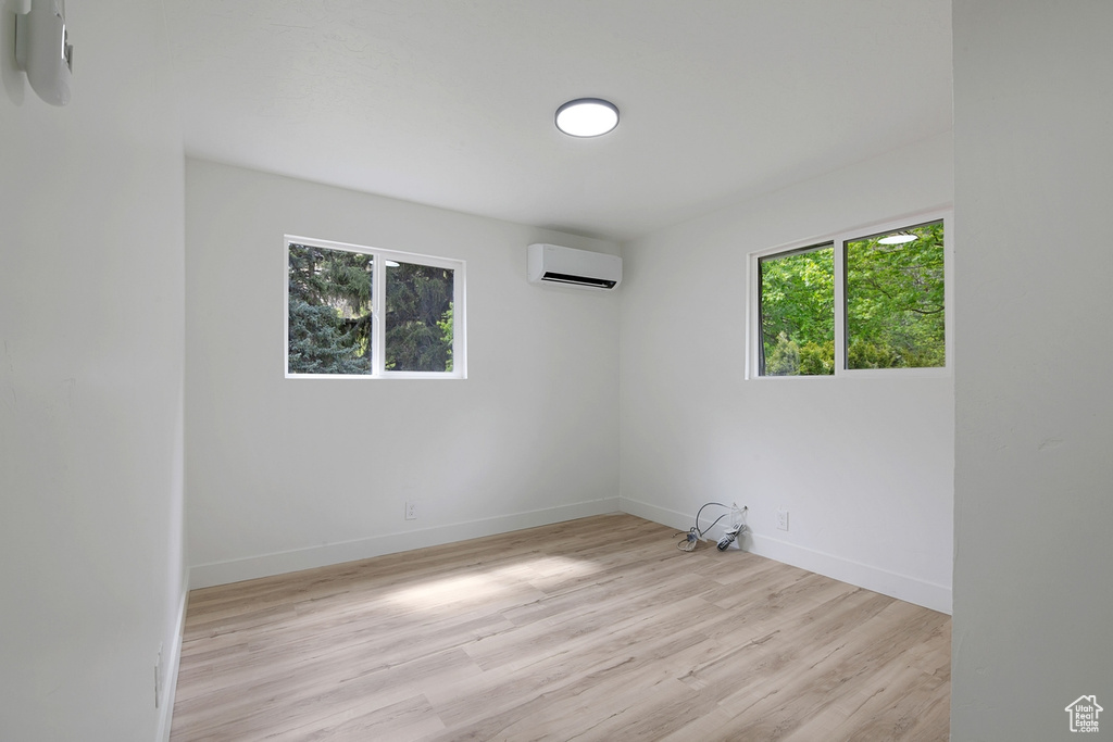 Unfurnished room featuring a wealth of natural light, light wood finished floors, baseboards, and a wall mounted air conditioner