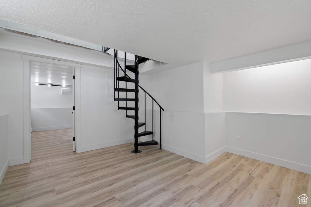 Finished basement featuring stairway, a textured ceiling, baseboards, and wood finished floors
