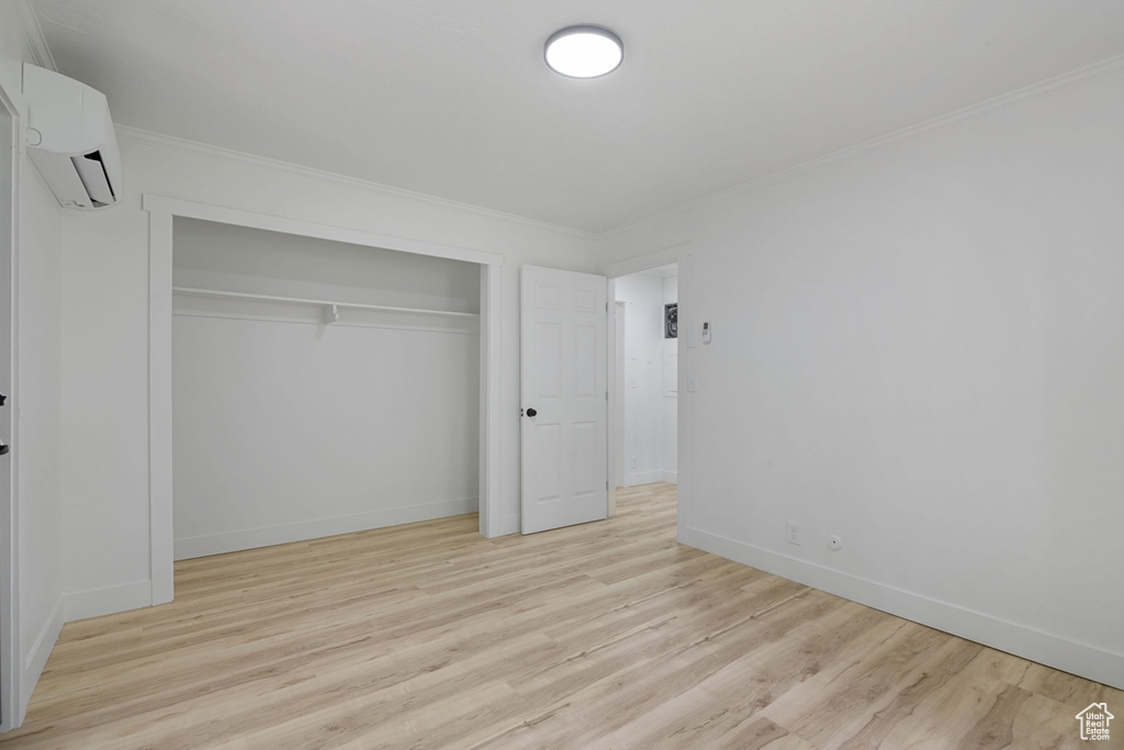 Unfurnished bedroom with light wood finished floors, a wall mounted AC, a closet, and ornamental molding