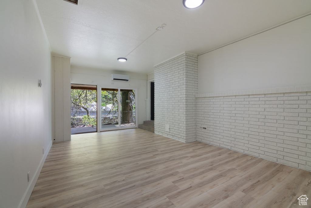 Empty room with a wall mounted air conditioner, wood finished floors, and brick wall