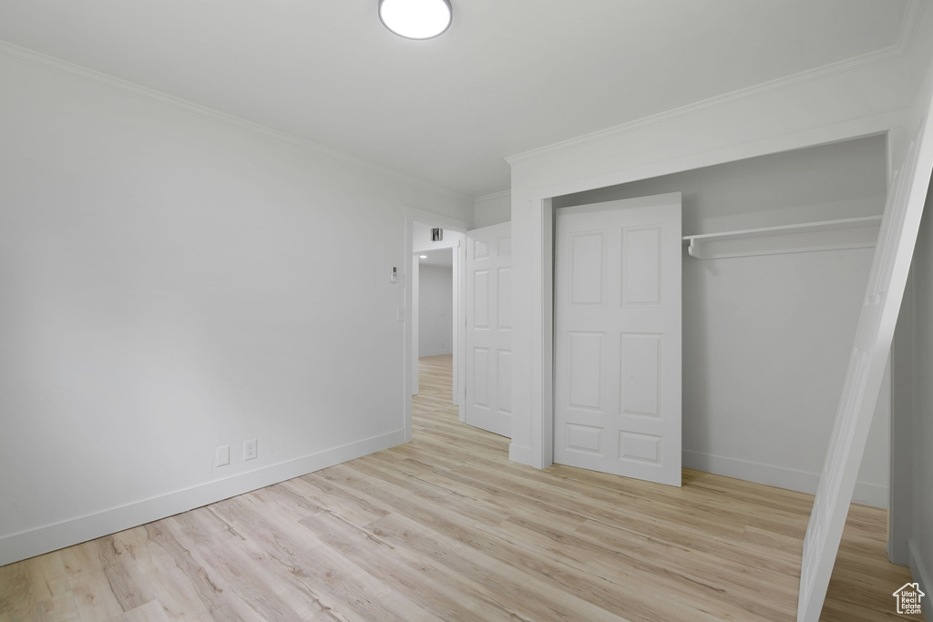 Unfurnished bedroom featuring a closet, baseboards, light wood-style floors, and crown molding