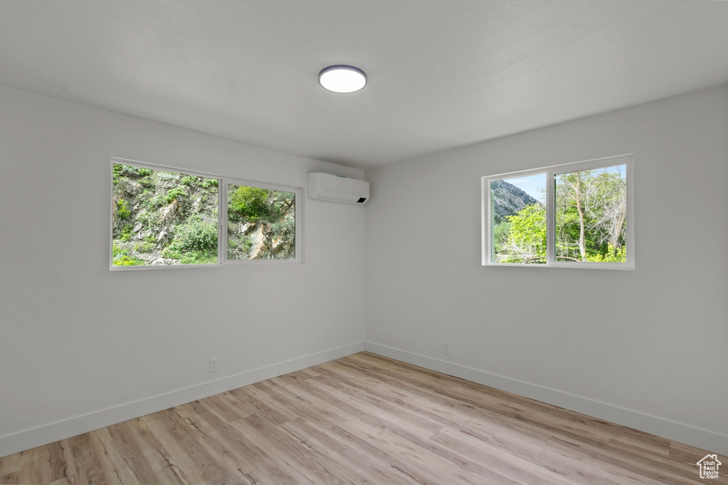 Empty room featuring light wood-type flooring, baseboards, a healthy amount of sunlight, and a wall unit AC
