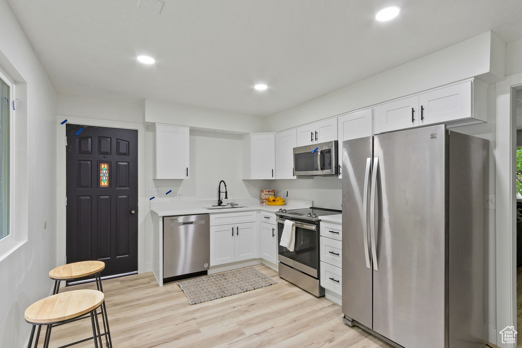 Kitchen featuring a sink, light countertops, white cabinets, appliances with stainless steel finishes, and light wood-type flooring