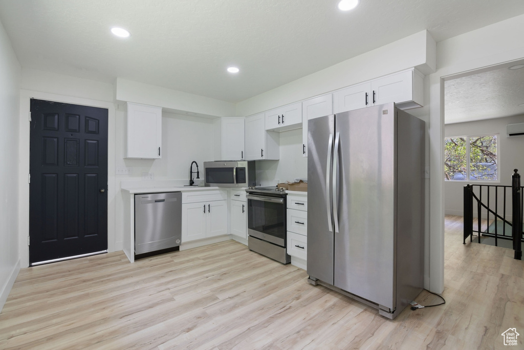 Kitchen featuring appliances with stainless steel finishes, white cabinetry, light countertops, and light wood-style floors