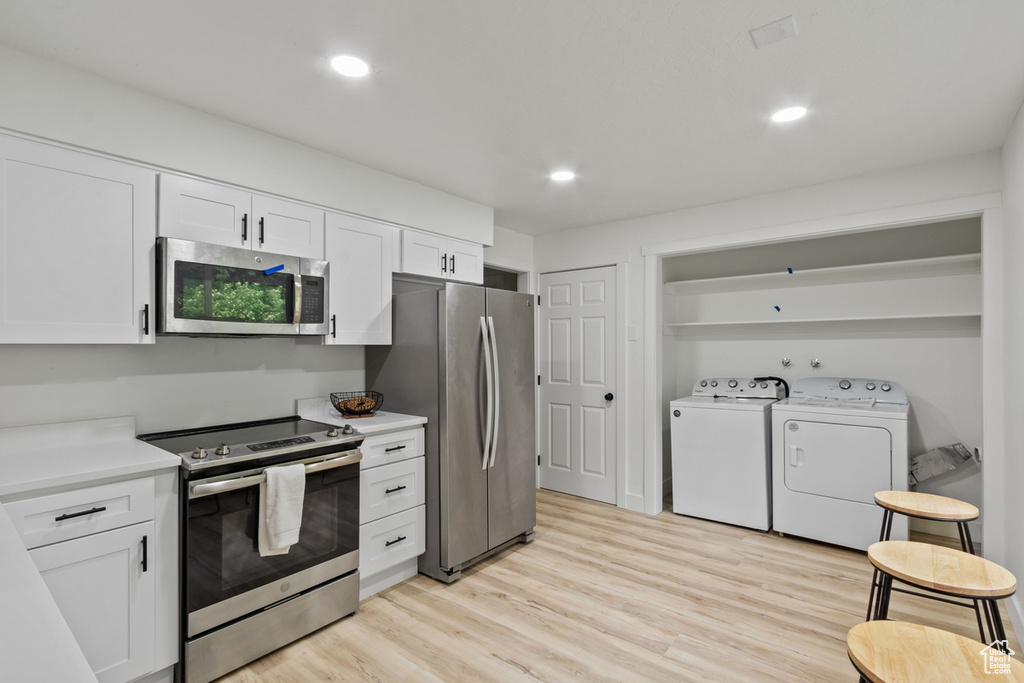 Kitchen with washer and dryer, stainless steel appliances, light wood finished floors, and white cabinetry
