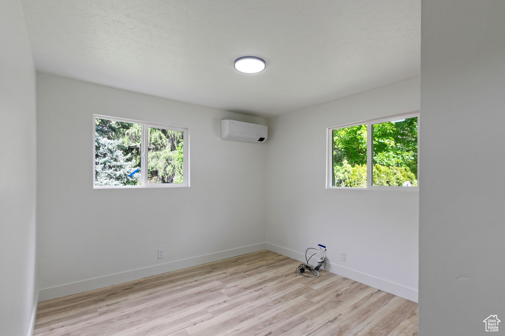 Empty room with plenty of natural light, a wall mounted AC, baseboards, and wood finished floors