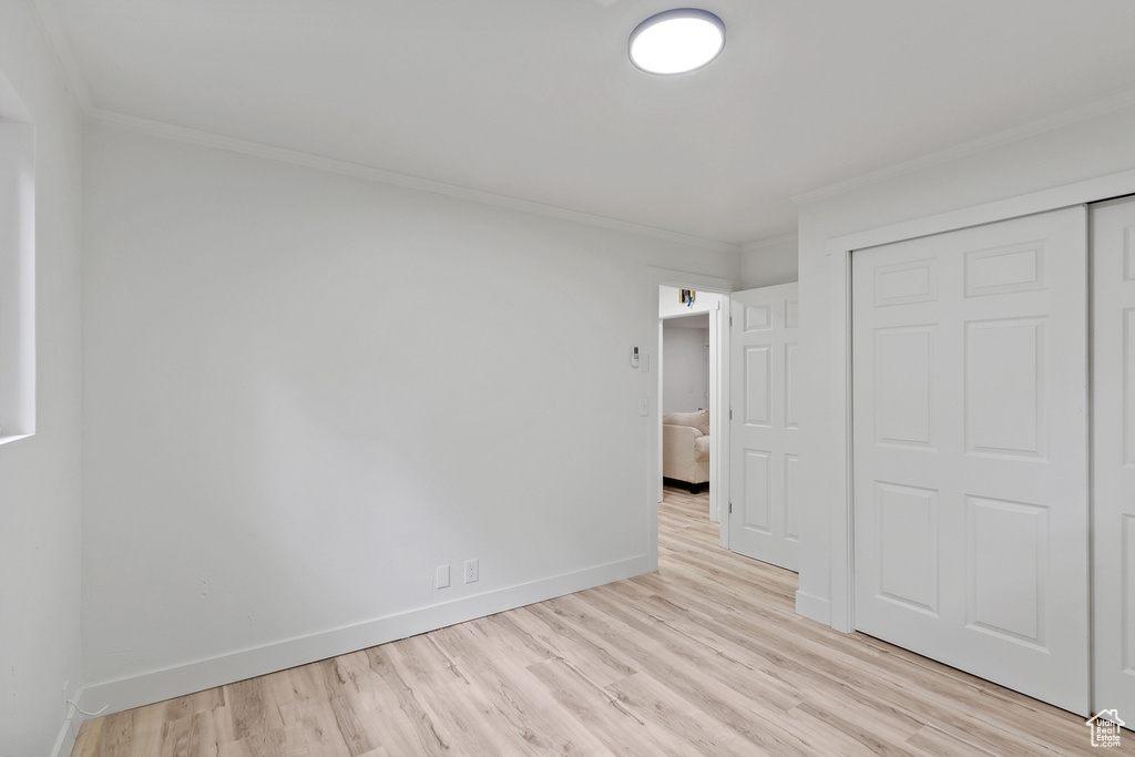 Unfurnished bedroom featuring light wood-style floors, baseboards, a closet, and ornamental molding