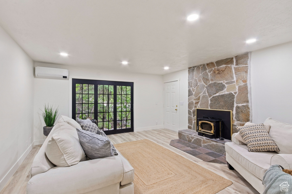 Living area with a wall unit AC, baseboards, light wood-style flooring, a wood stove, and recessed lighting