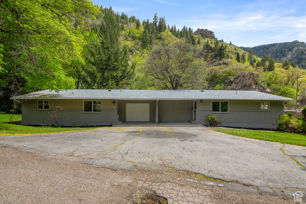 Ranch-style house featuring brick siding, an attached carport, aphalt driveway, a chimney, and a garage