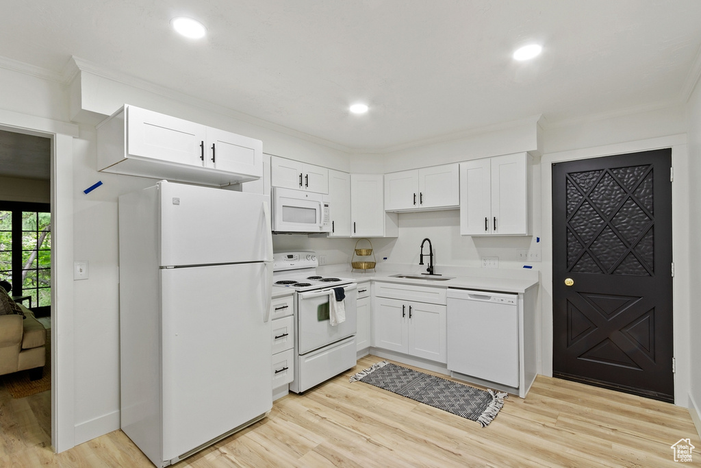 Kitchen with white appliances, white cabinets, light wood-style floors, and a sink