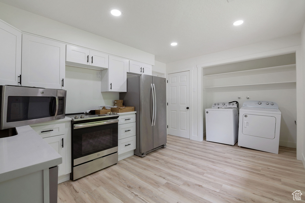 Kitchen featuring light wood-style flooring, light countertops, white cabinets, appliances with stainless steel finishes, and washer and clothes dryer