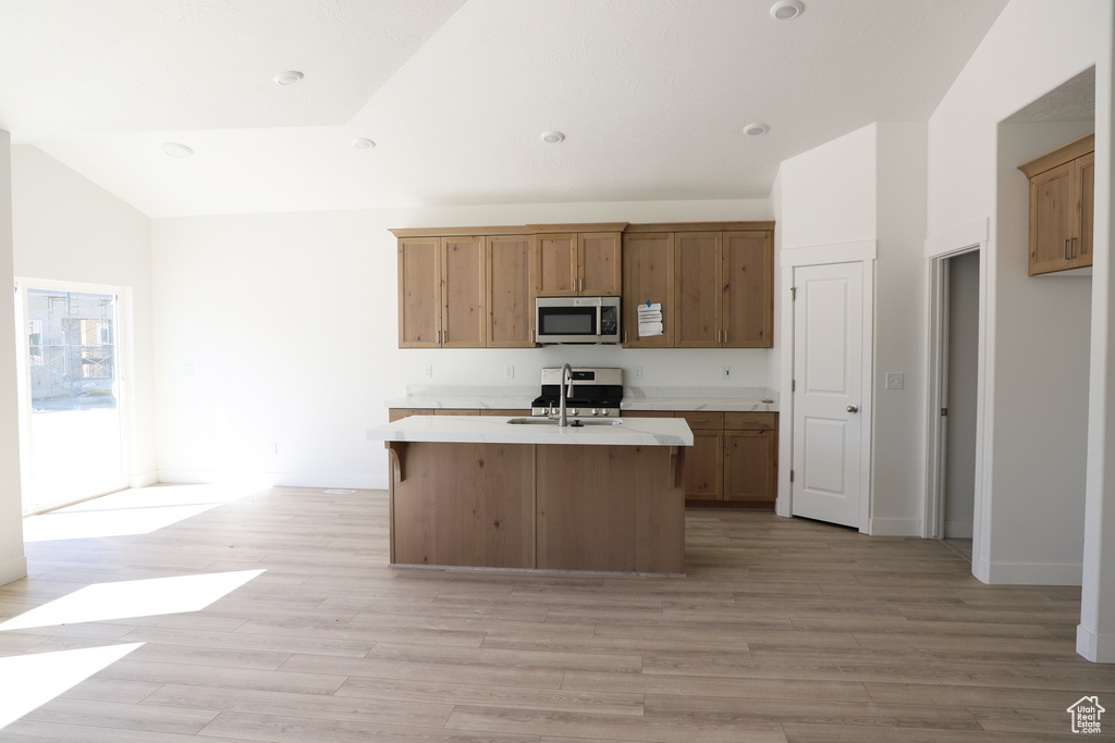 Kitchen with stainless steel microwave, light countertops, a kitchen island with sink, light wood-type flooring, and lofted ceiling