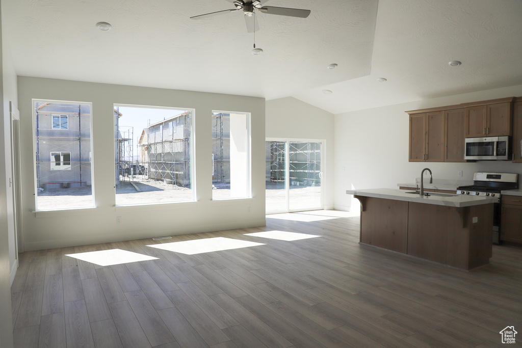 Kitchen featuring stainless steel appliances, ceiling fan, vaulted ceiling, wood finished floors, and open floor plan