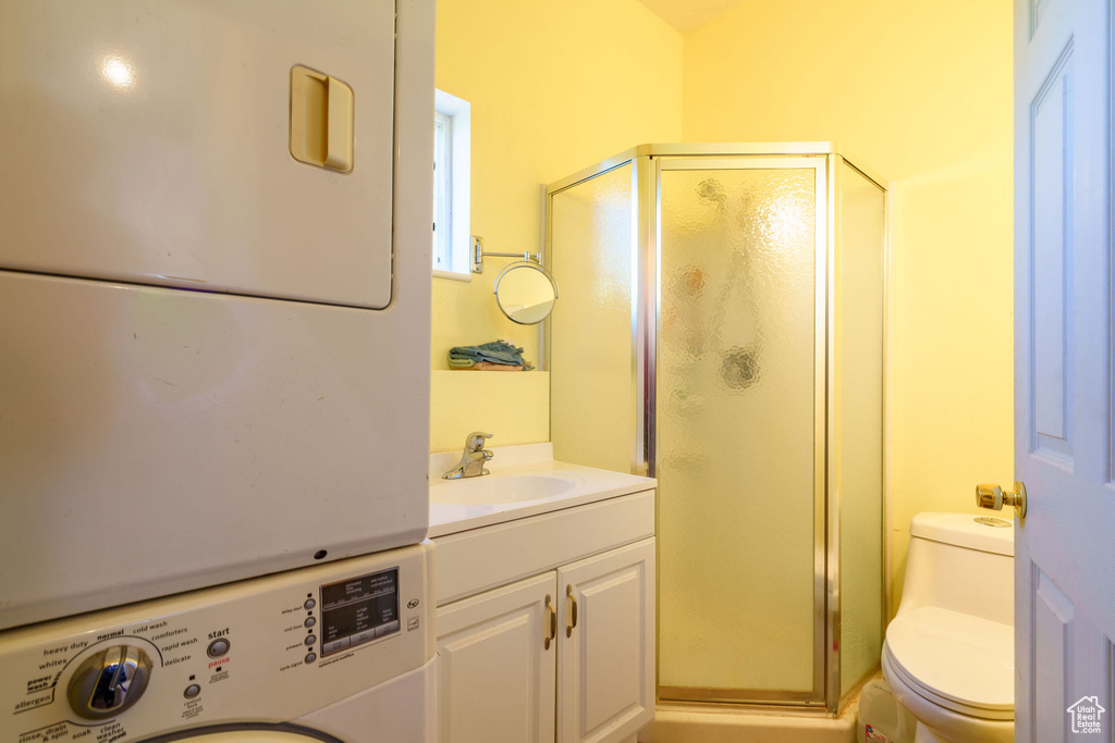 Bathroom with a stall shower, toilet, vanity, and stacked washer and dryer