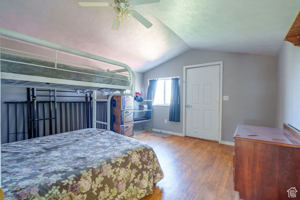 Bedroom featuring wood finished floors, baseboards, ceiling fan, vaulted ceiling, and a textured ceiling