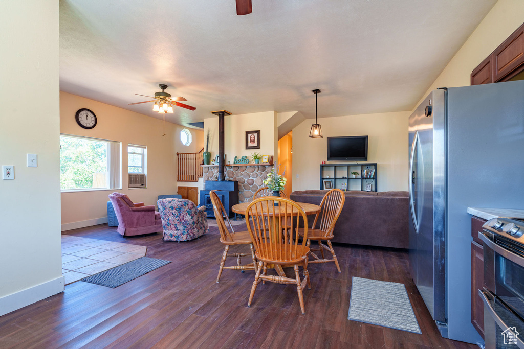 Dining area with dark wood-type flooring, baseboards, a wood stove, and ceiling fan