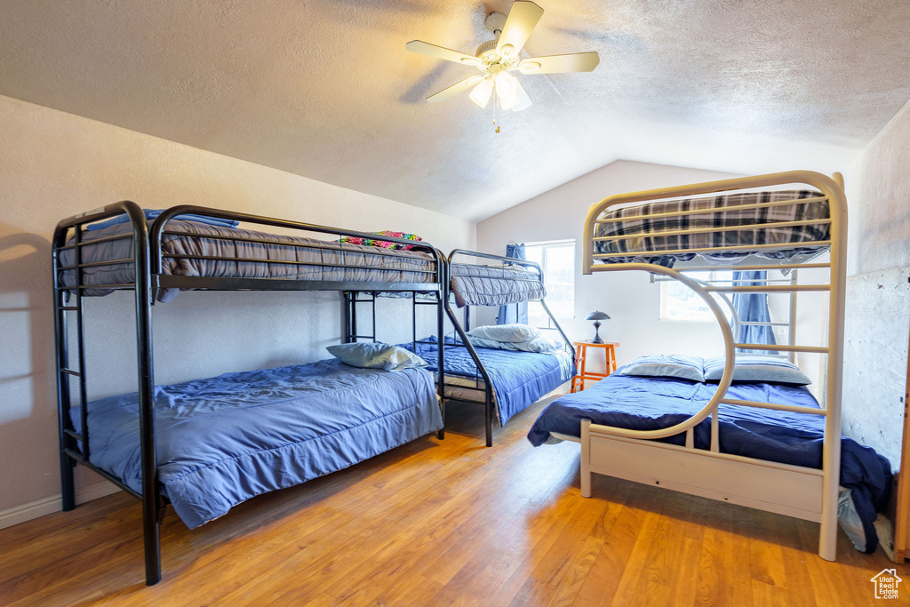 Bedroom featuring ceiling fan, lofted ceiling, wood finished floors, and a textured ceiling