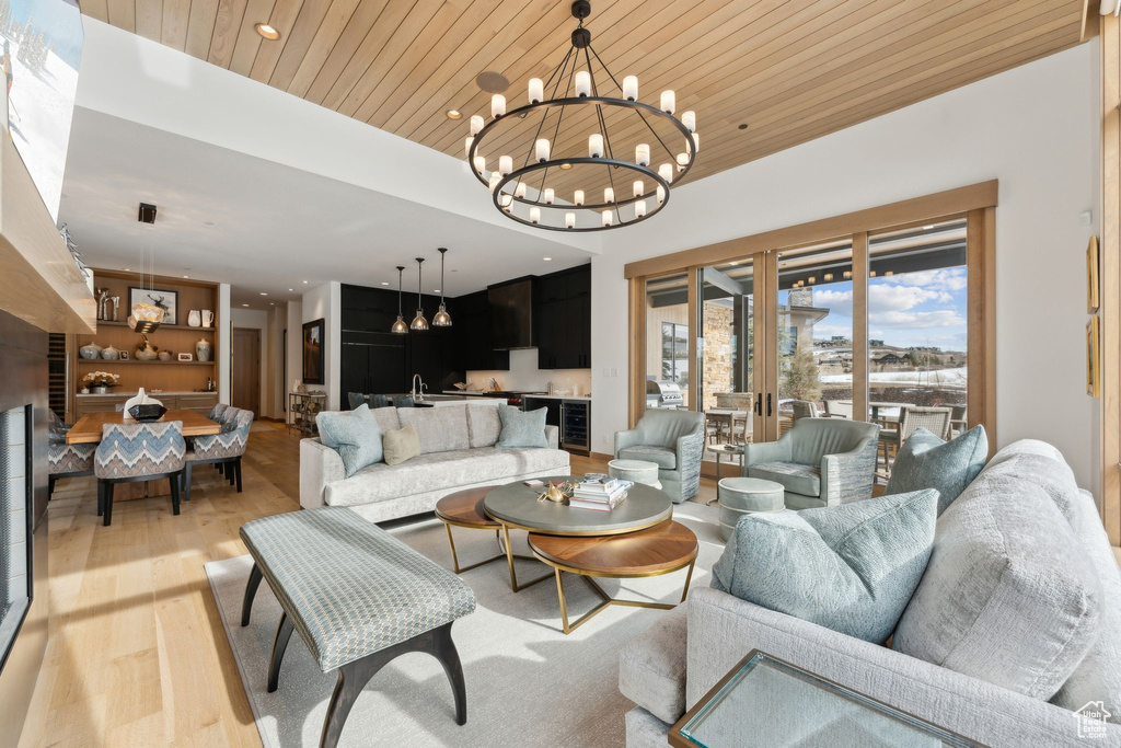 Living room with beverage cooler, light wood-style flooring, wood ceiling, and an inviting chandelier