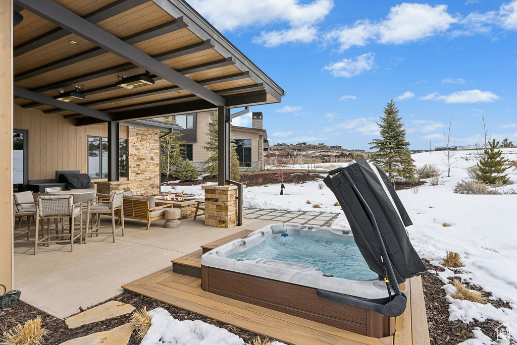 Snow covered deck with an outdoor living space, hot tub deck surround, and a patio area