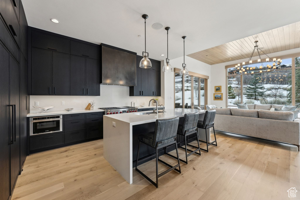 Kitchen with light countertops, a kitchen breakfast bar, light wood-style floors, custom exhaust hood, and a sink
