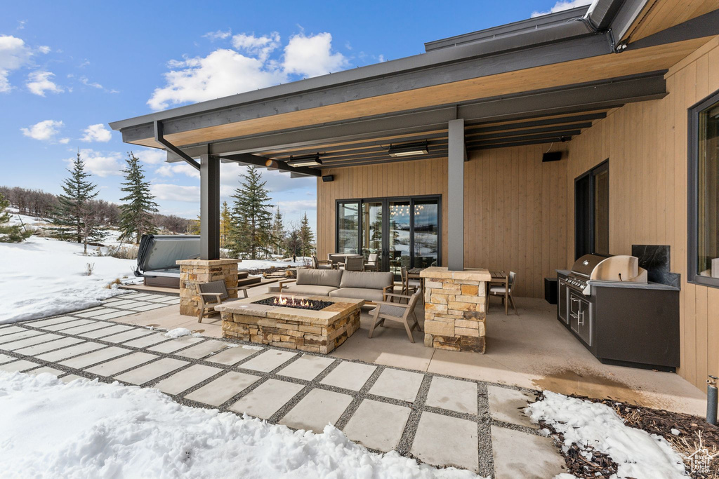Snow covered patio featuring grilling area, an outdoor kitchen, and an outdoor fire pit