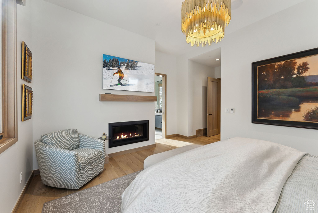 Bedroom featuring a glass covered fireplace, baseboards, an inviting chandelier, and wood finished floors
