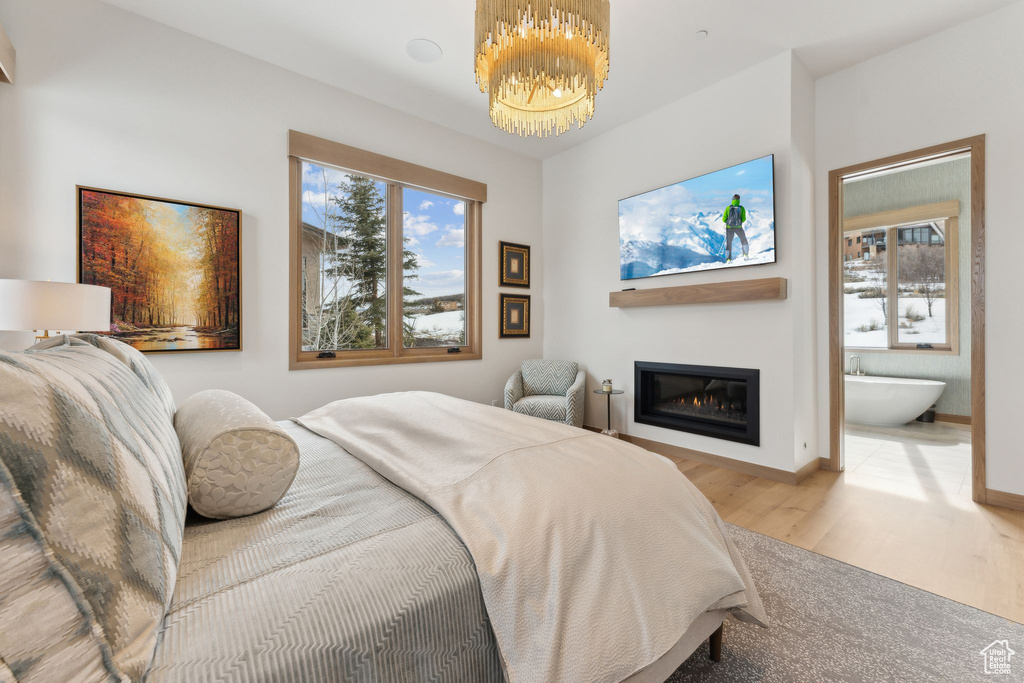 Bedroom with connected bathroom, baseboards, an inviting chandelier, wood finished floors, and a glass covered fireplace