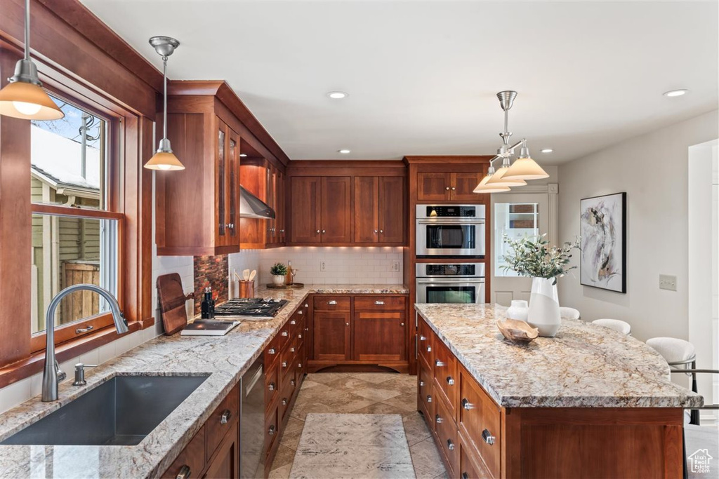 Kitchen featuring a center island, light stone countertops, decorative backsplash, stainless steel appliances, and a sink