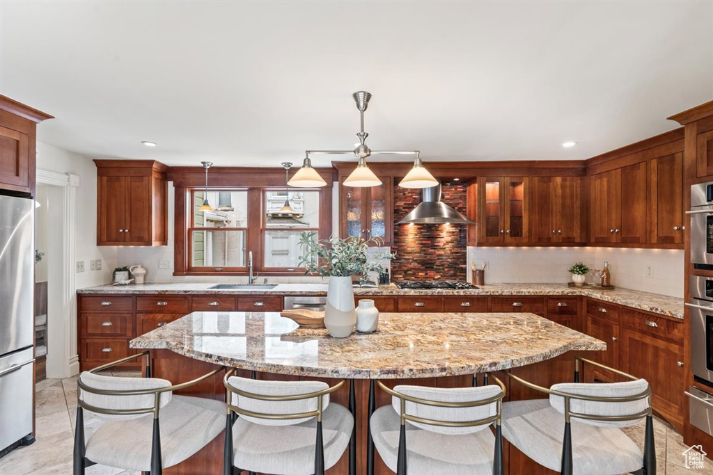 Kitchen featuring tasteful backsplash, a center island, wall chimney range hood, appliances with stainless steel finishes, and a sink