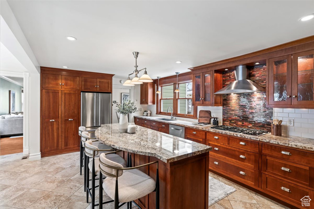 Kitchen with decorative backsplash, a sink, appliances with stainless steel finishes, wall chimney exhaust hood, and glass insert cabinets