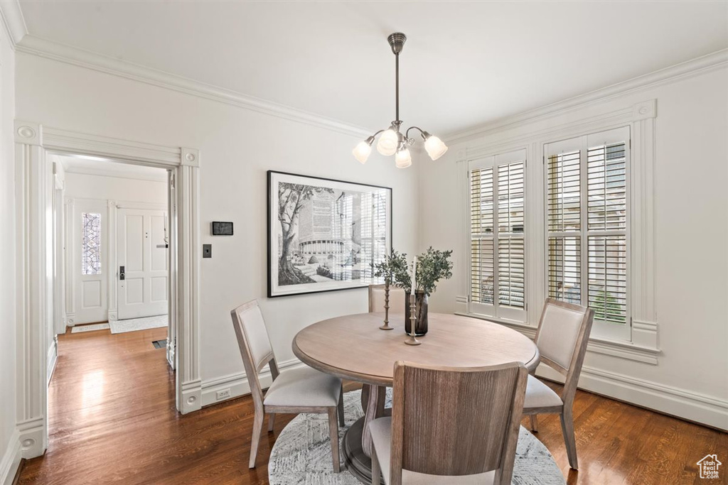 Dining area featuring dark wood finished floors, a notable chandelier, baseboards, and ornamental molding