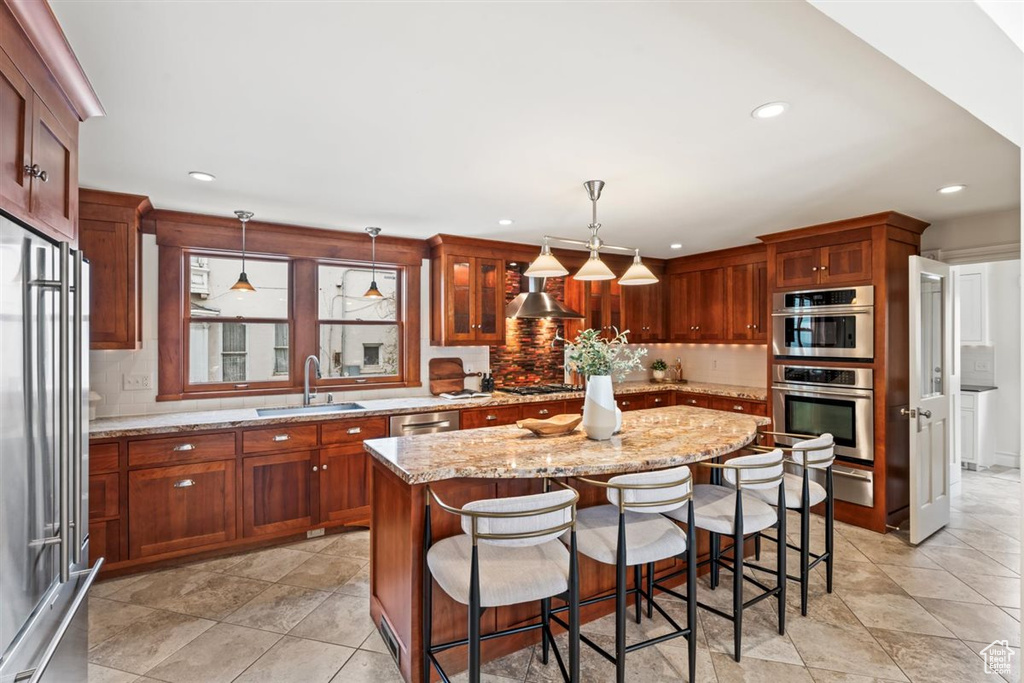 Kitchen featuring a center island, light stone counters, decorative backsplash, appliances with stainless steel finishes, and a sink