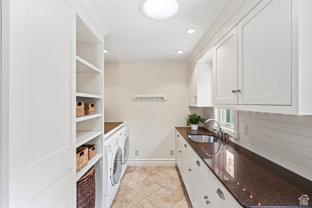 Clothes washing area featuring a sink, washing machine and dryer, cabinet space, light tile patterned floors, and baseboards