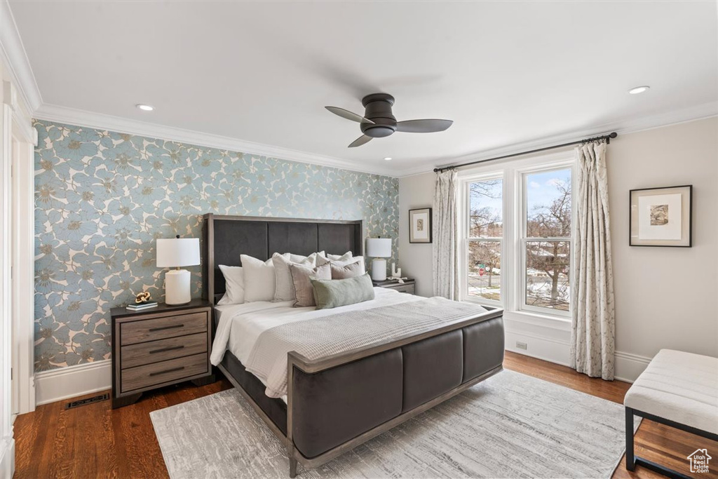 Bedroom with wood finished floors, crown molding, and wallpapered walls