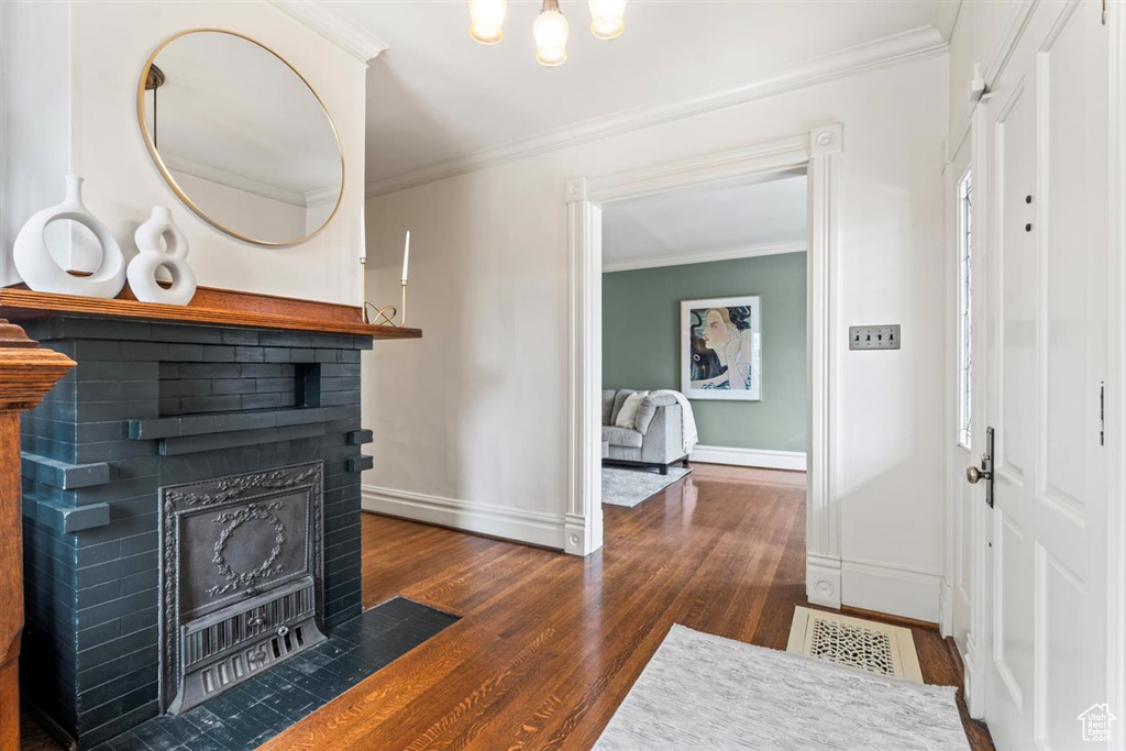 Foyer entrance with dark wood finished floors, visible vents, a brick fireplace, and ornamental molding