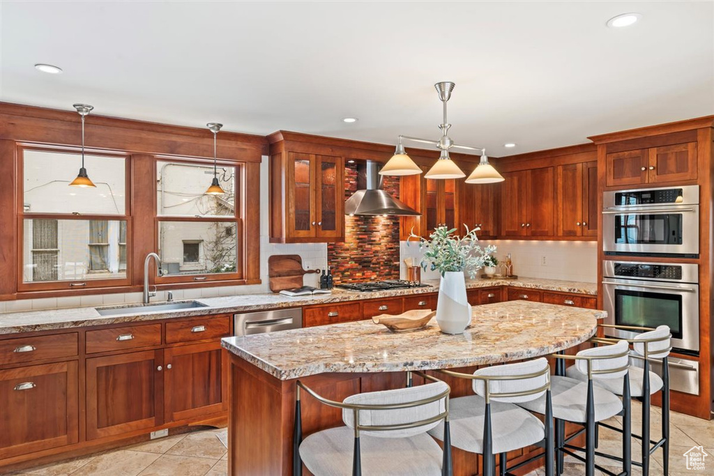 Kitchen featuring a sink, appliances with stainless steel finishes, a kitchen bar, wall chimney exhaust hood, and backsplash