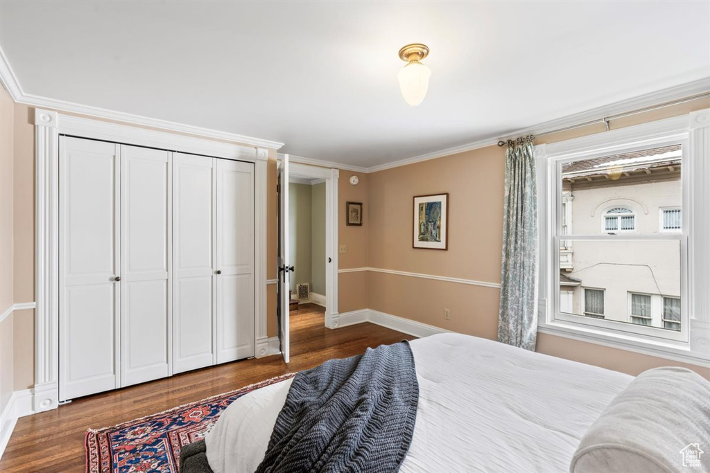 Bedroom with a closet, baseboards, wood finished floors, and ornamental molding