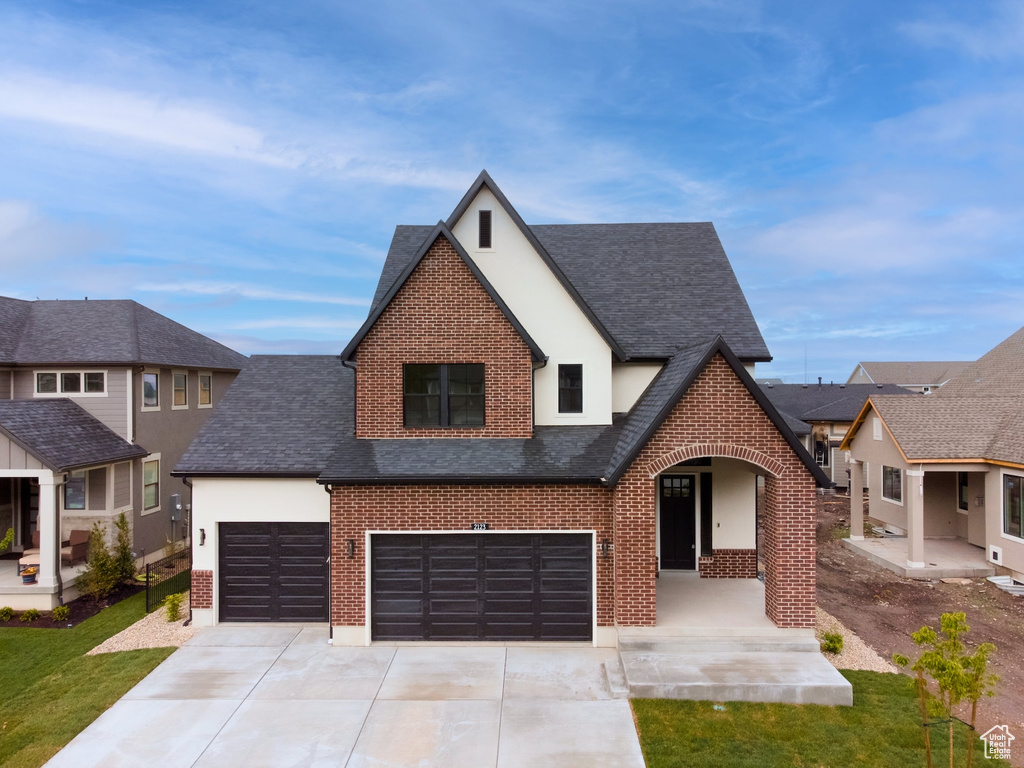 View of front of property featuring brick siding, roof with shingles, stucco siding, and concrete driveway