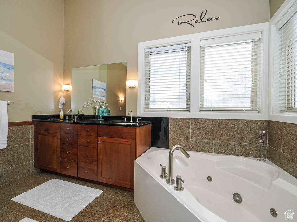 Bathroom with a sink, granite finish floor, tile walls, double vanity, and a whirlpool tub