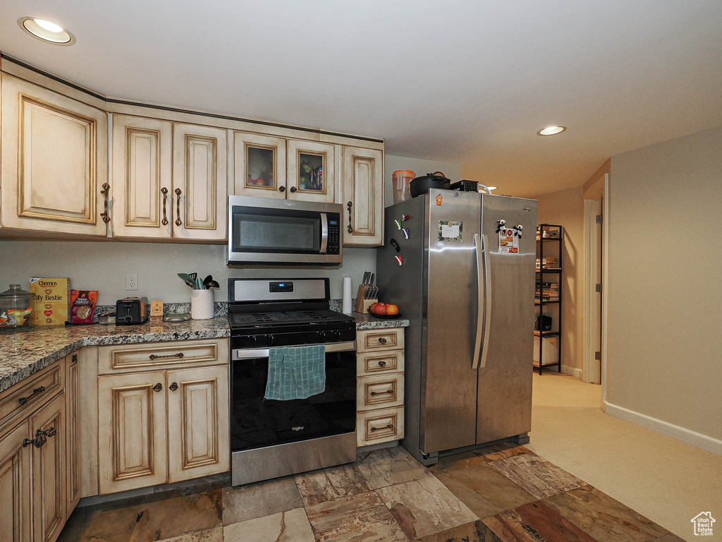 Kitchen with glass insert cabinets, baseboards, recessed lighting, cream cabinetry, and stainless steel appliances