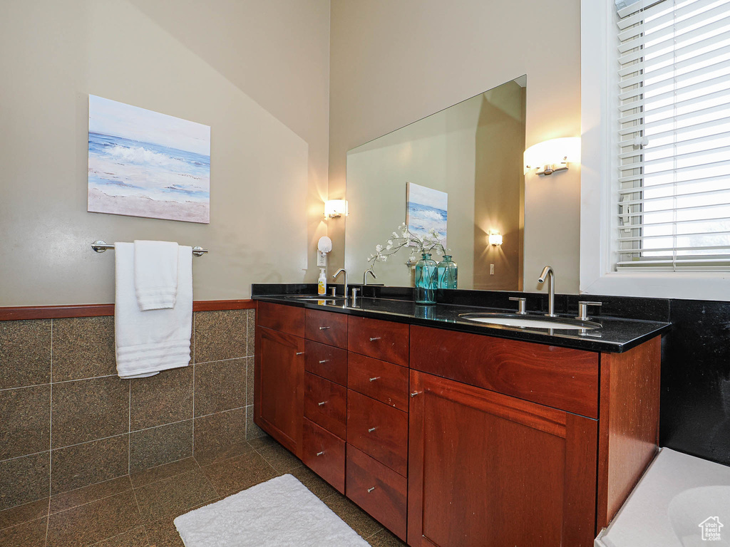 Full bathroom featuring double vanity, a wainscoted wall, tile walls, and a sink