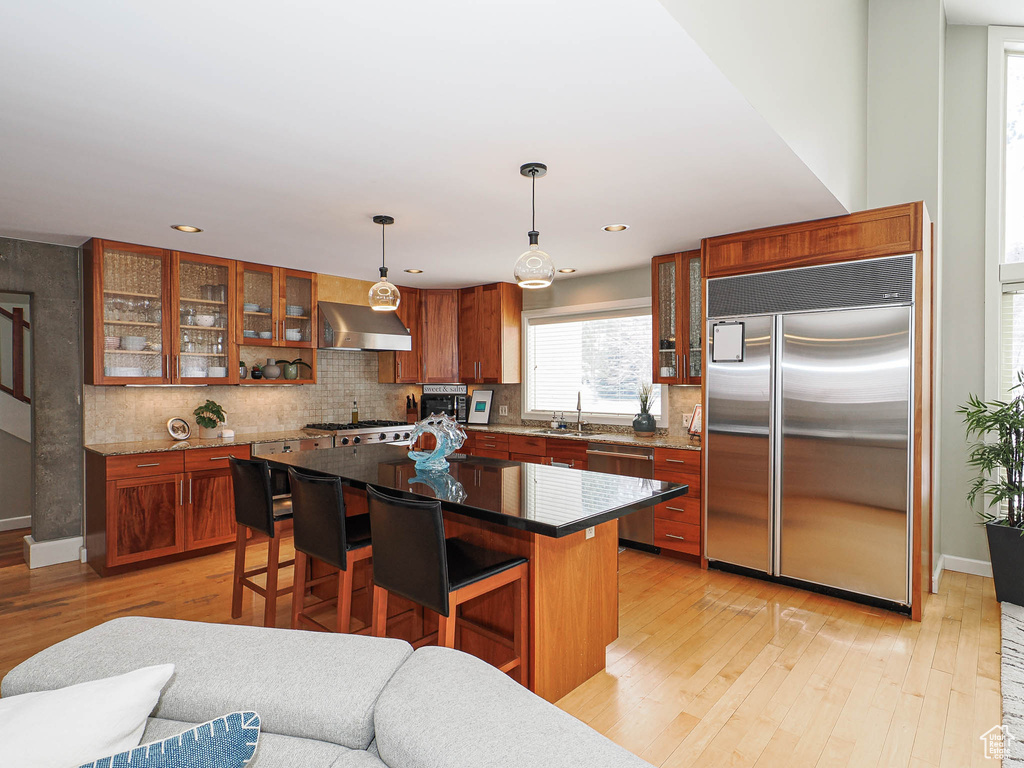 Kitchen with light wood-type flooring, a sink, stainless steel appliances, wall chimney range hood, and brown cabinets