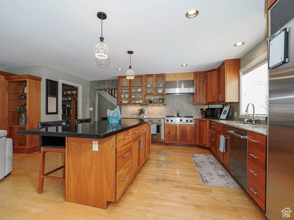 Kitchen with light wood-style flooring, a sink, a kitchen breakfast bar, stainless steel appliances, and wall chimney range hood