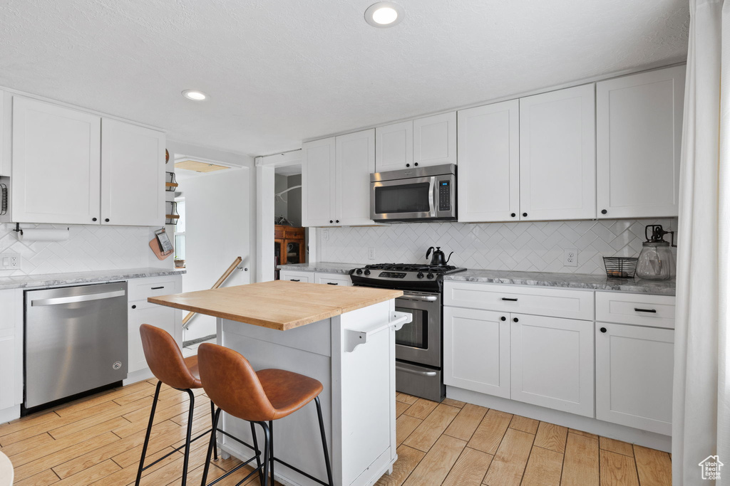 Kitchen with stainless steel appliances, a breakfast bar, white cabinets, and light wood finished floors